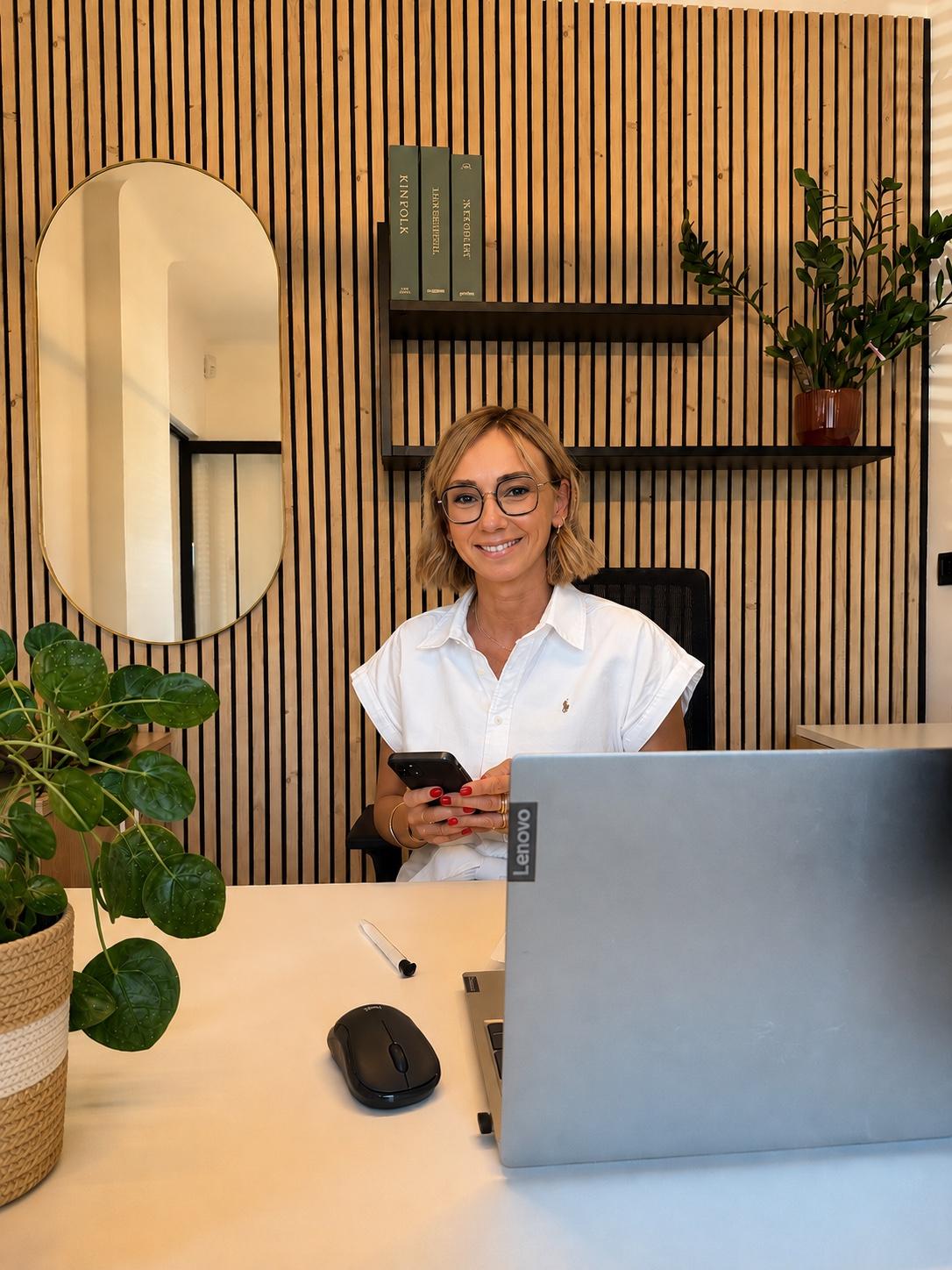 Stéphanie Widart, souriante, installée à son bureau dans un espace lumineux aux tons bois et végétal